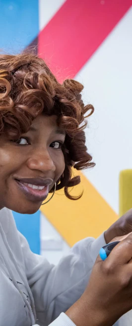 Student in a white hoodie using a screwdriver to adjust components on a blue robotic vehicle during a hands-on computing activity. Student in a white hoodie using a screwdriver to adjust components on a blue robotic vehicle during a hands-on computing activity.